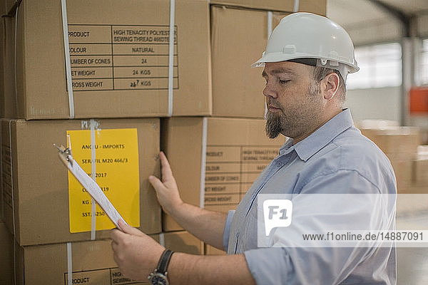 Mann mit Schutzhelm kontrolliert Lieferung in der Fabrik