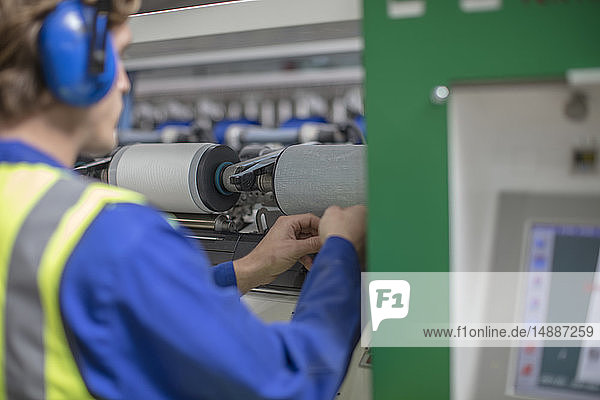 Mann mit Ohrenschützern bei der Arbeit am Spulenautomaten in der Fabrik