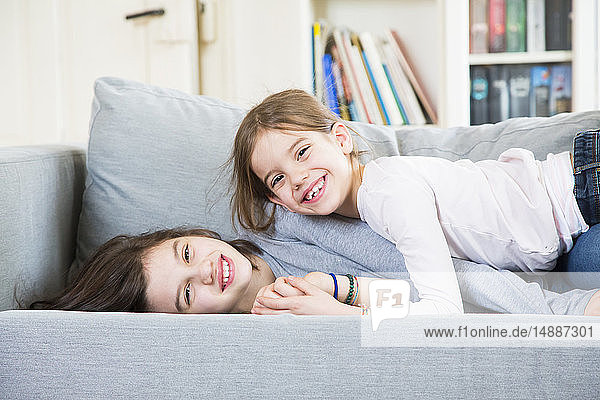 Porträt von zwei glücklichen Schwestern  die auf der Couch kuscheln