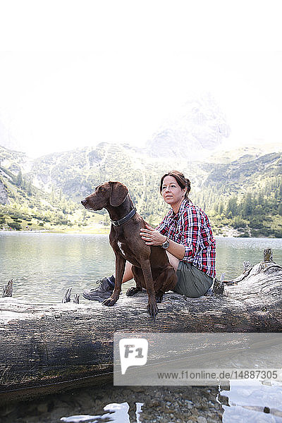 Austria  Tyrol  woman with dog sitting on tree trunk at lake Seebensee