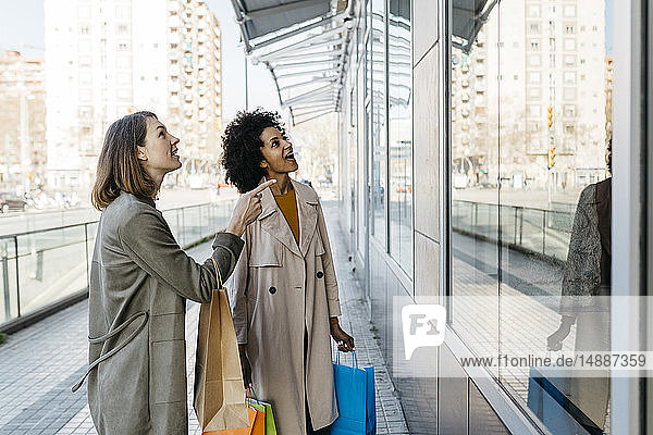 Zwei aufgeregte Frauen mit Einkaufstaschen schauen auf Schaufenster in der Stadt