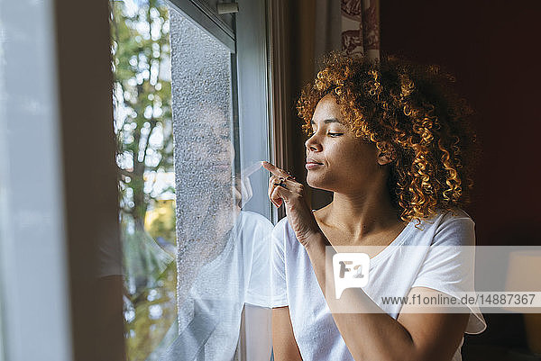 Junge Frau mit lockigem Haar schreibt mit dem Finger auf Fensterscheibe