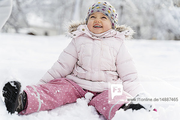 Süßes kleines Mädchen sitzt im Winter im Schnee