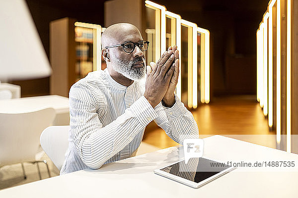 Porträt eines nachdenklichen reifen Mannes am Schreibtisch in einer Bibliothek mit digitalem Tablett