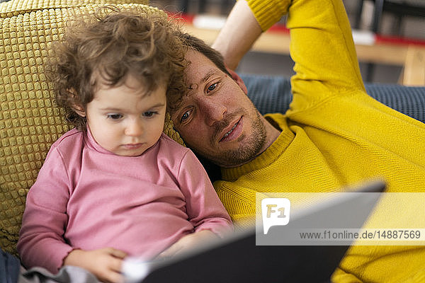 Vater und Tochter liegen auf der Couch und schauen einen Film auf dem Tablett