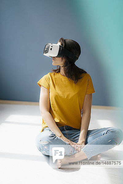 Frau sitzt im Schneidersitz auf dem Boden und trägt eine VR-Brille