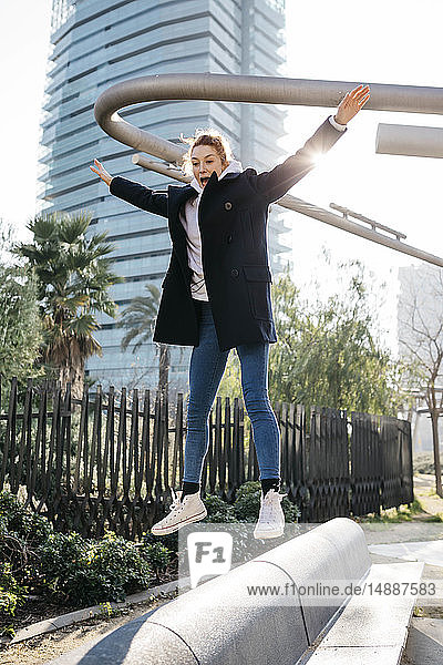 Young woman balancing and jumping on a city bench
