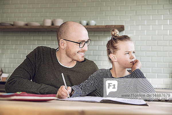 Father and daughter sitting in kitchen  doing homework