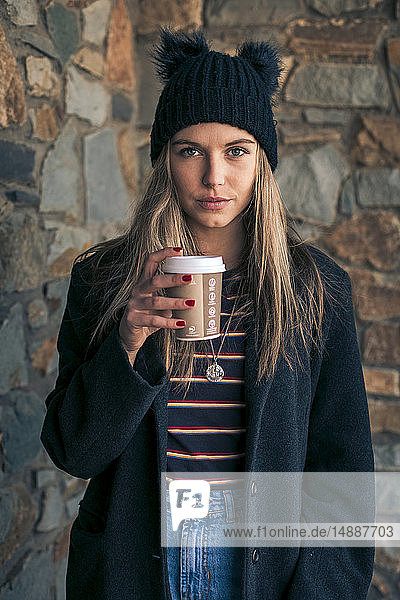 Porträt einer jungen Frau mit Kaffee zum Mitnehmen in Mantel und Wollmütze