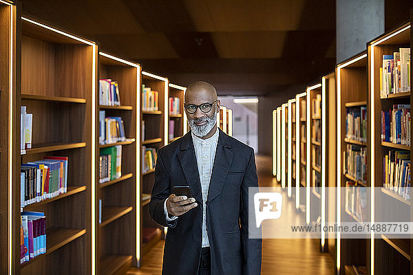 Porträt eines lächelnden Geschäftsmannes mit Smartphone in der Bibliothek