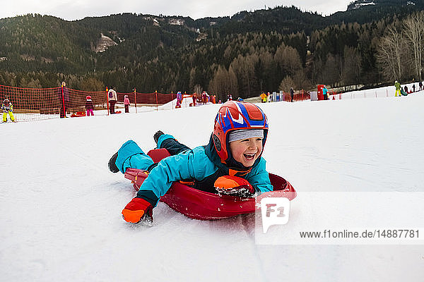 Italien  Trentino-Südtirol  glücklicher Junge auf rodelndem Plastikschlitten
