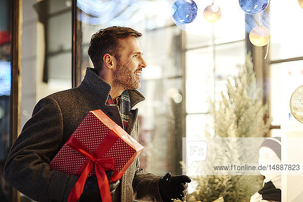 Smiling man with Christmas present looking in shop window