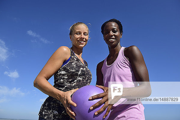 Porträt von zwei lächelnden Frauen  die unter blauem Himmel einen Fitnessball halten