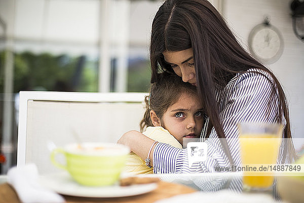 Mutter umarmt ihre traurige Tochter beim Frühstück zu Hause