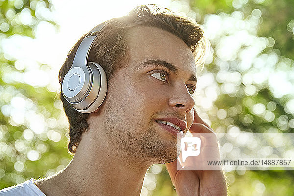 Lächelnder junger Mann mit Kopfhörern  der draußen Musik hört
