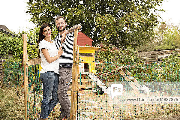 Portrait of confident couple standing at chickenhouse in garden