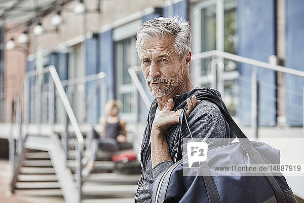 Portrait of mature man with sports bag in front of gym