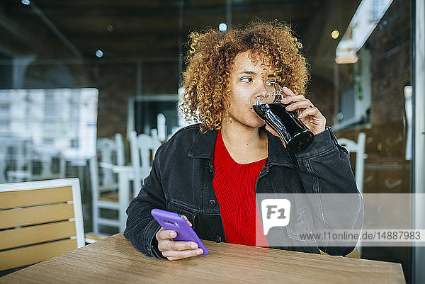 Junge Frau mit Handy trinkt Cola in einer Bar