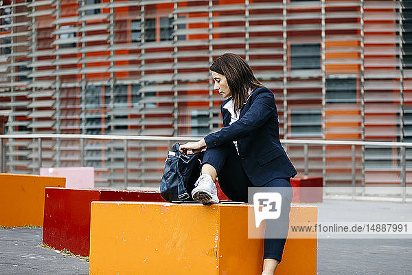 Geschäftsfrau  die vor einem Bürogebäude in der Stadt sitzt und etwas in der Tasche sucht