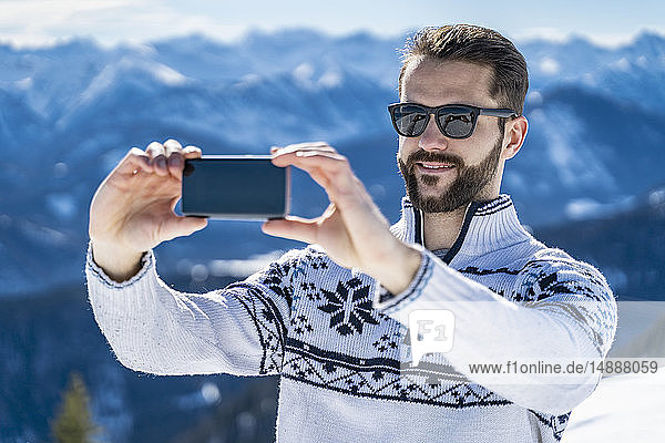 Deutschland  Bayern  Brauneck  Mann im Winter in den Bergen beim Selfie