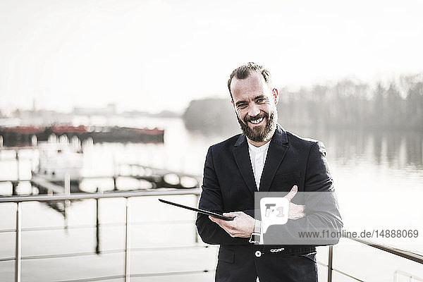 Lachender Geschäftsmann steht auf einem Hausboot und hält ein digitales Tablett