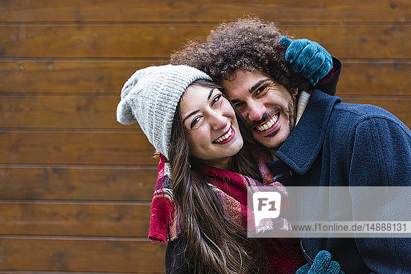 Portrait of happy young couple in winterwear hugging in front of wooden wall