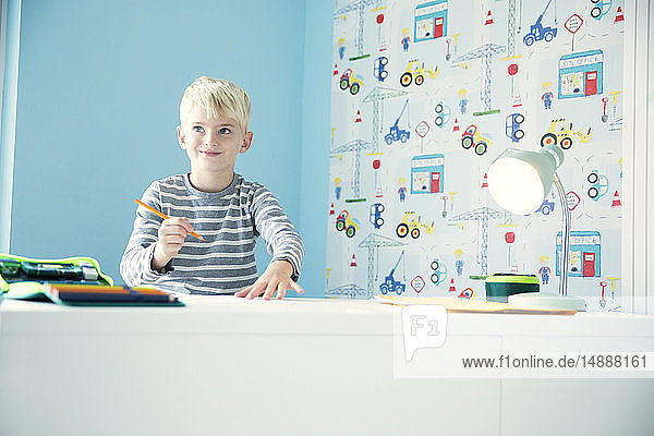 Lächelnder Junge macht Hausaufgaben am Schreibtisch im Kinderzimmer