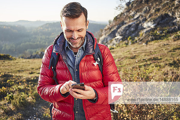 Lächelnder Mann auf einer Wanderung in den Bergen beim Handy-Check