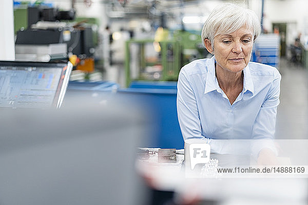 Porträt einer leitenden Geschäftsfrau in einer Fabrik  die ein Werkstück betrachtet