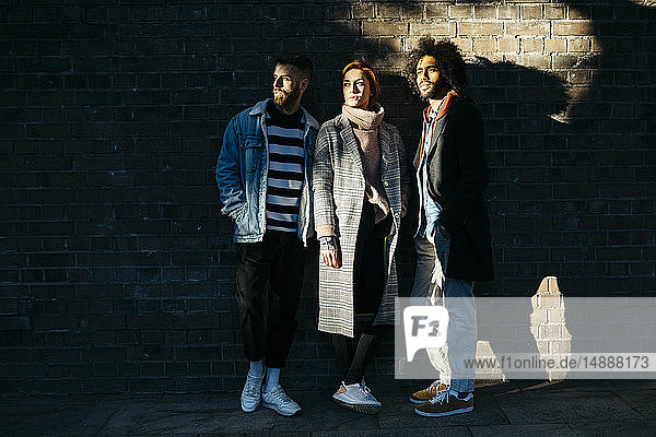 Drei ernsthafte Freunde stehen im Schatten an einer Ziegelmauer