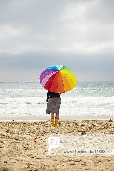 Frau mit buntem Sonnenschirm am Strand sitzend