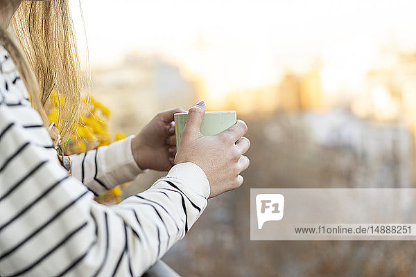 Junge Frau auf Balkon mit Tasse Kaffee  Teilansicht