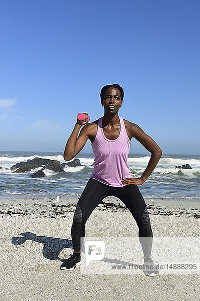 Woman doing fitness exercise with dumbbell on the beach