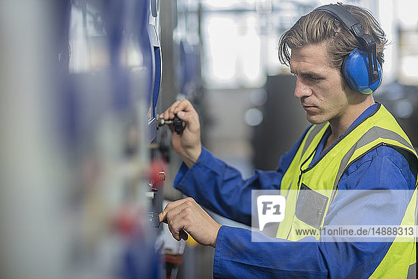 Mann trägt Gehörschützer bei der Bedienung einer Maschine in einer Fabrik