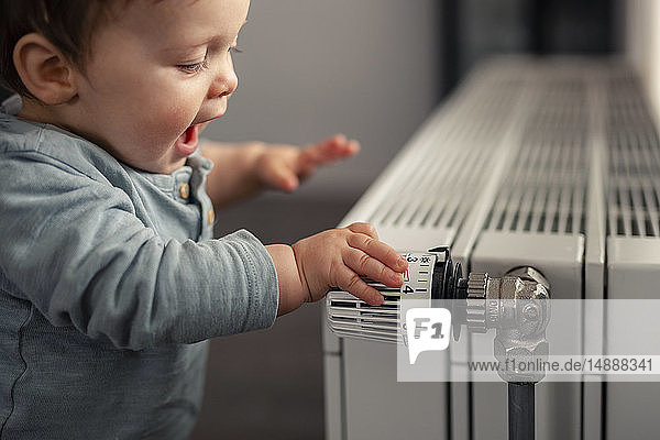 Aufgeregter kleiner Junge spielt mit dem Thermostat einer Heizung