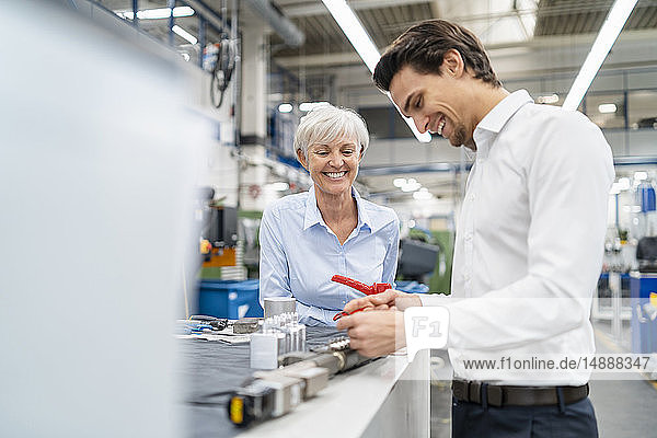 Happy businessman and senior businesswoman examining workpiece in a factory