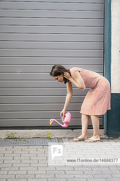 Frau gießt Pflanzen mit einer Flamingokanne in einer städtischen Straße
