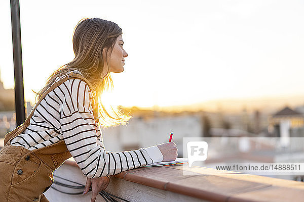 Junge Frau macht bei Sonnenuntergang Notizen auf der Dachterrasse