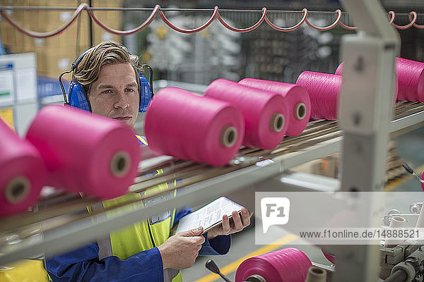 Mann mit Ohrenschützern bei der Arbeit am Spulenautomaten in der Fabrik