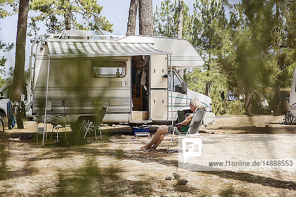 Frankreich  Gironde  Frau sitzt vor einem Wohnmobil auf einem Campingplatz und benutzt ein digitales Tablett