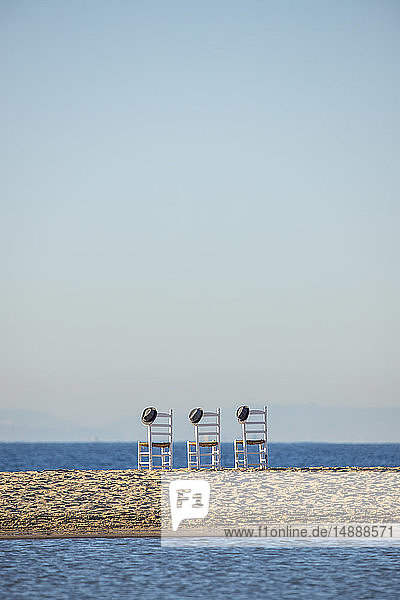 Drei leere Stühle mit Hüten nebeneinander vor dem Meer