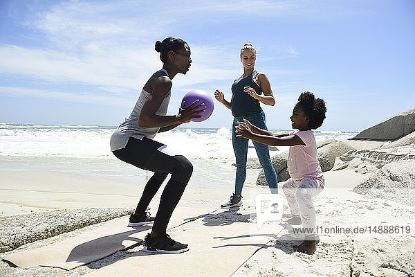 Mutter mit Tochter und Freund trainieren mit einem Ball am Strand