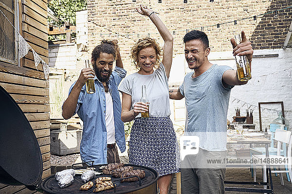 Freunde beim Grillen im Hinterhof  bei der Zubereitung von Fleisch auf dem Grill