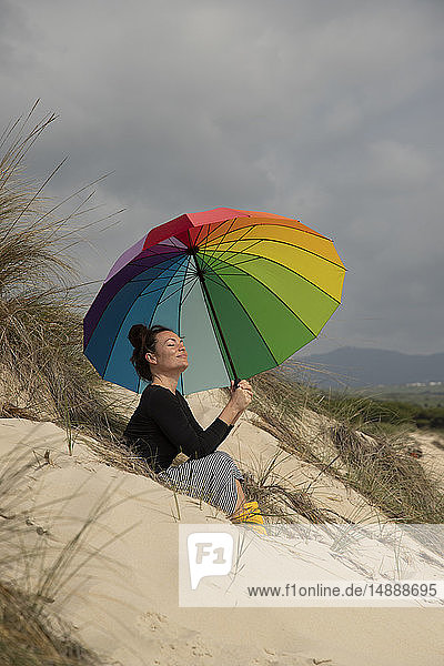 Frau mit buntem Sonnenschirm am Strand sitzend  sonnenbadend