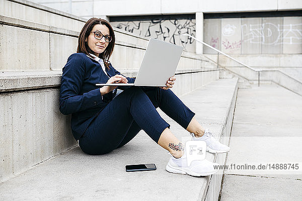 Porträt einer Geschäftsfrau  die mit einem Laptop im Freien auf einer Treppe sitzt
