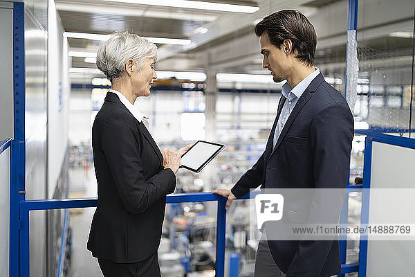 Businessman and senior businesswoman with tablet talking in a factory