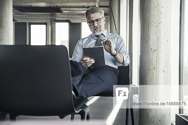 Reifer Geschäftsmann auf Stuhl sitzend mit Tablett