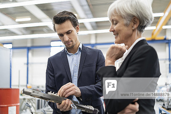 Lächelnder Geschäftsmann und leitende Geschäftsfrau bei der Untersuchung eines Werkstücks in einer Fabrik