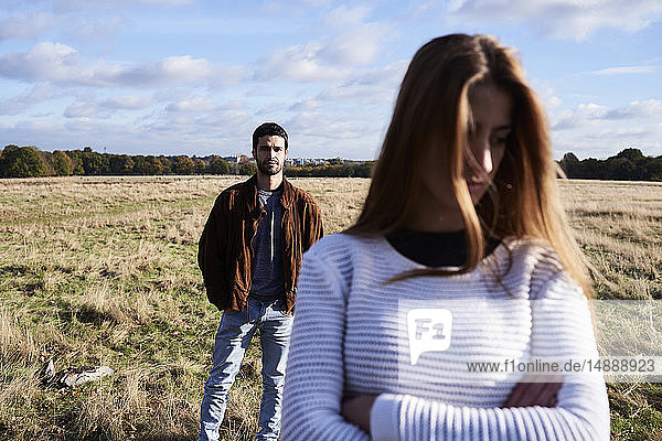 Seriöse junge Frau steht auf einem Feld mit einem Mann hinter ihr