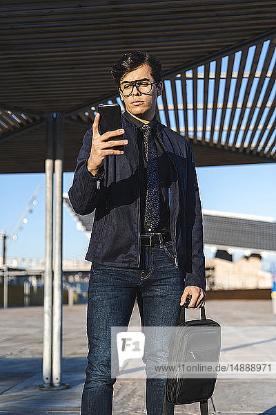 Porträt eines modischen jungen Geschäftsmannes mit Rucksack beim Blick auf das Handy